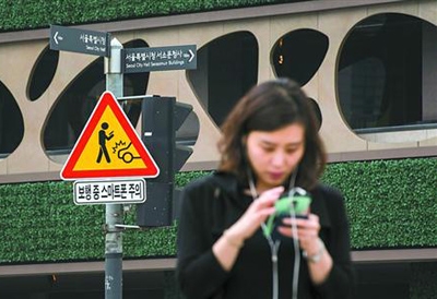 韩国首尔，市中心一个十字路口树立的警示牌提醒行人注意安全，不要光低头看手机